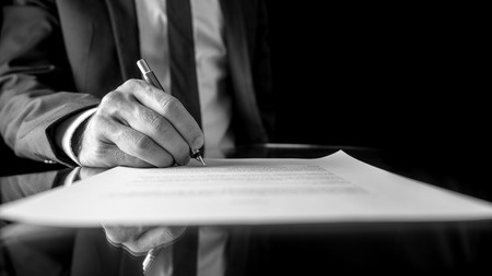 29990721-black-and-white-low-angle-image-of-the-hand-of-a-businessman-in-a-suit-signing-a-document-or-contrac